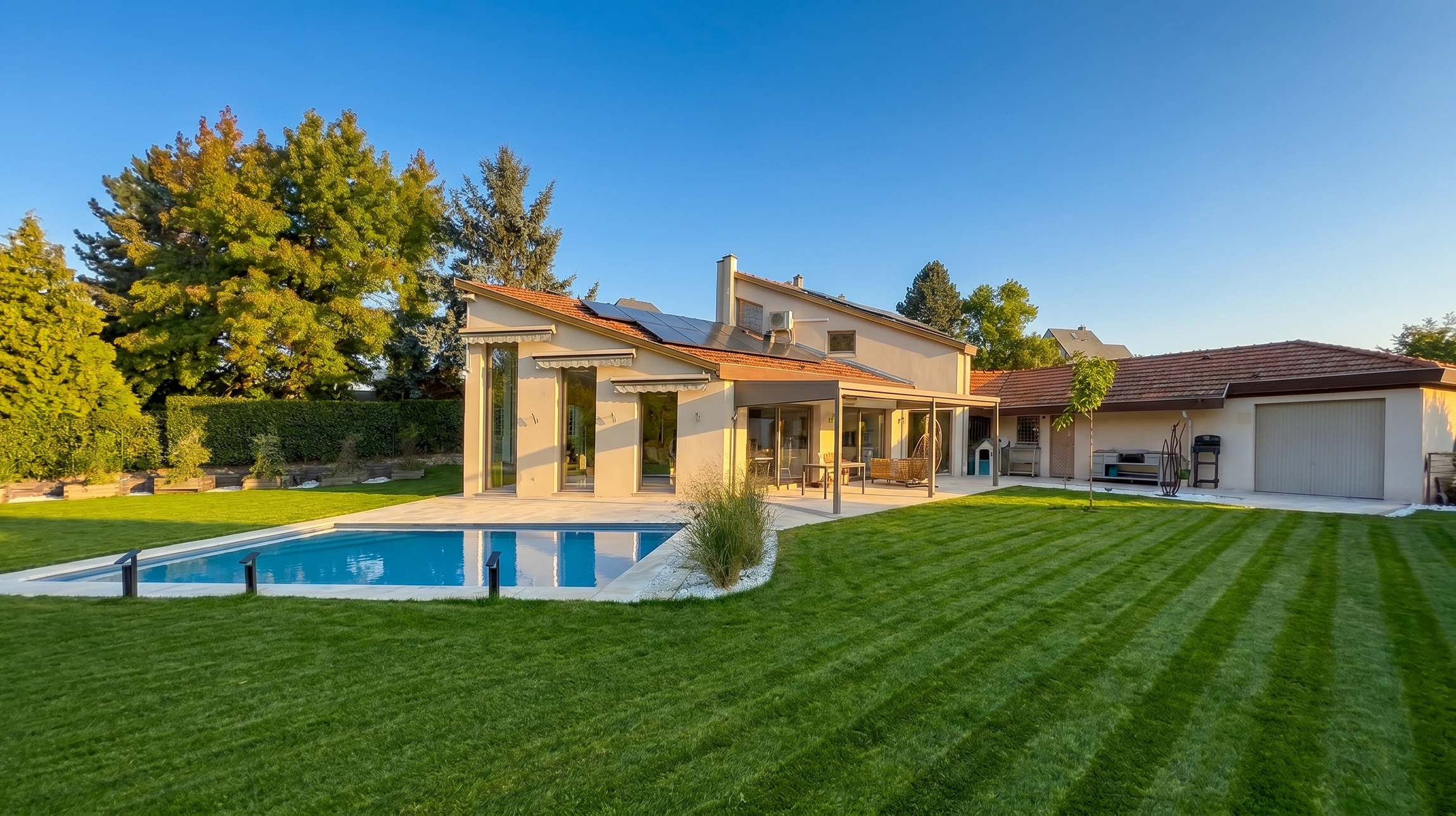 Jardin résidentiel moderne avec terrasse en dalles de béton, bordures paysagères en paillis noir, pelouse tondue et plantation d'arbustes conifères le long d'une clôture en bois